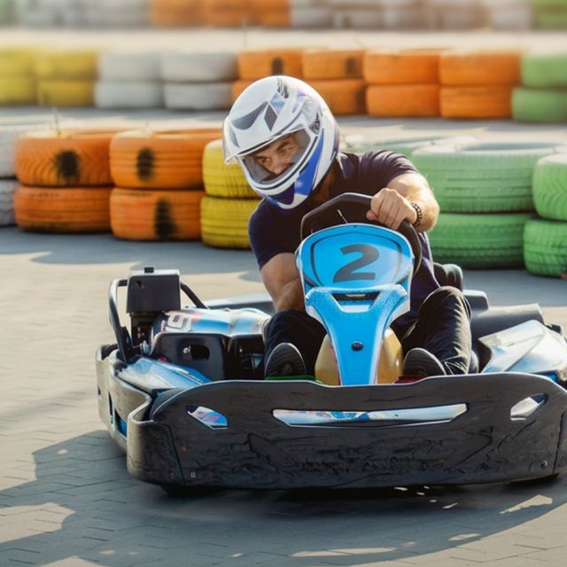 A person in a blue go-kart, marked with the number two, wears a helmet while racing on a track.