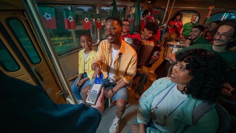 Passenger making contactless Visa payment onboard a lively group bus ride.