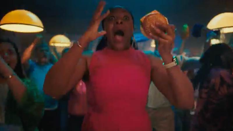 Excited football fan holding a burger while celebrating in a lively restaurant during match viewing.